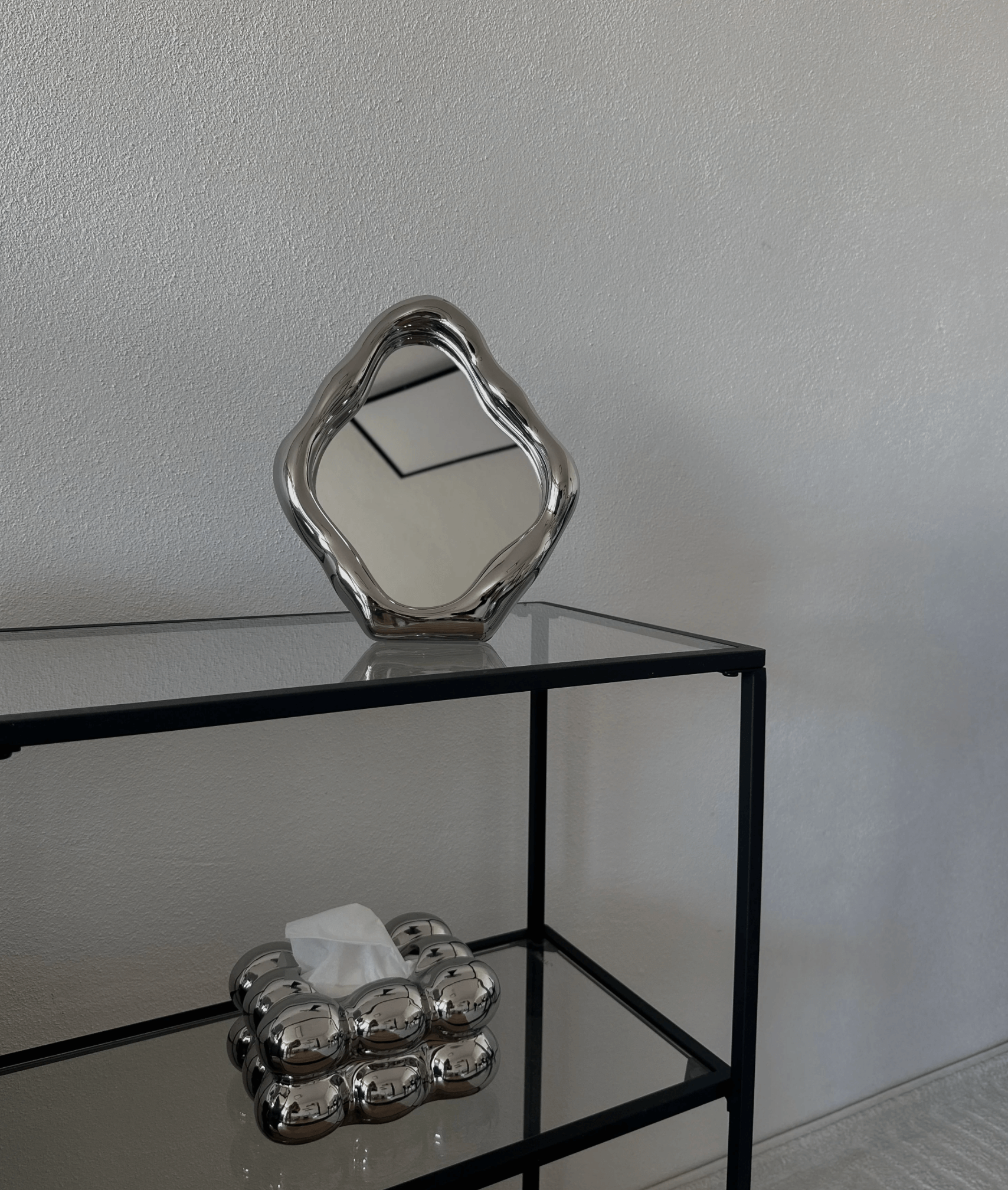 Elegant freestanding table mirror with a unique wavy design on a modern black shelf, showcasing stylish decor.