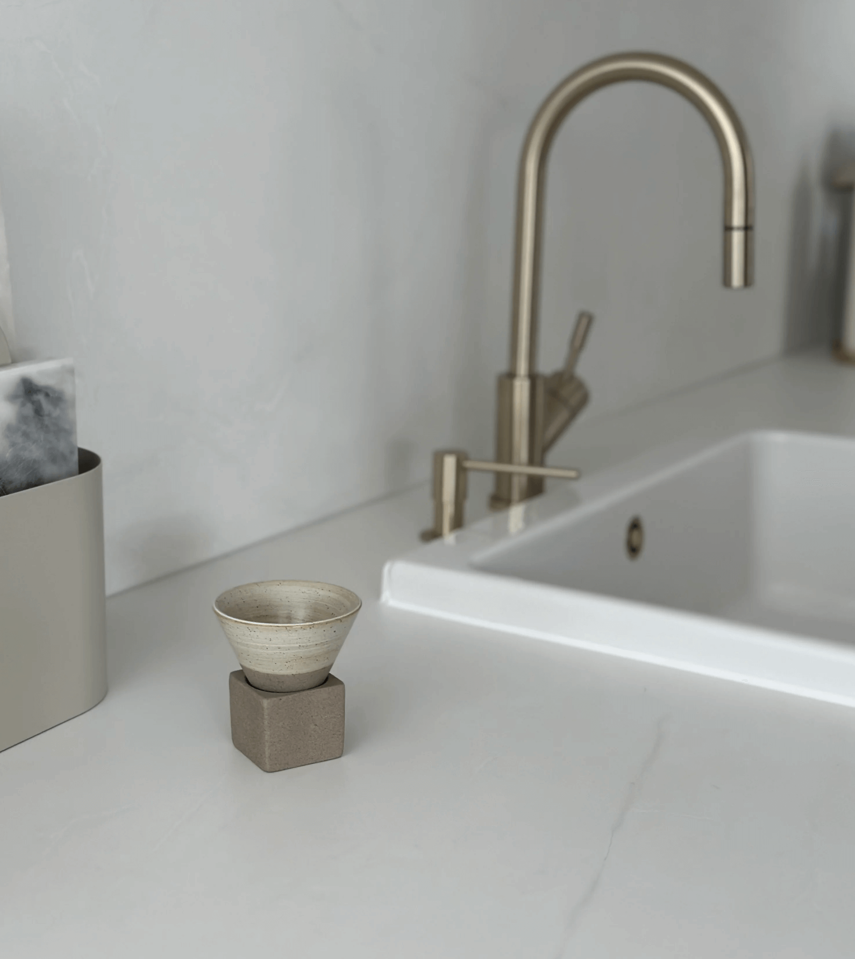 Japanische Keramik-Teetasse mit einzigartigem Design neben modernem Wasserhahn auf weißem Küchentresen.