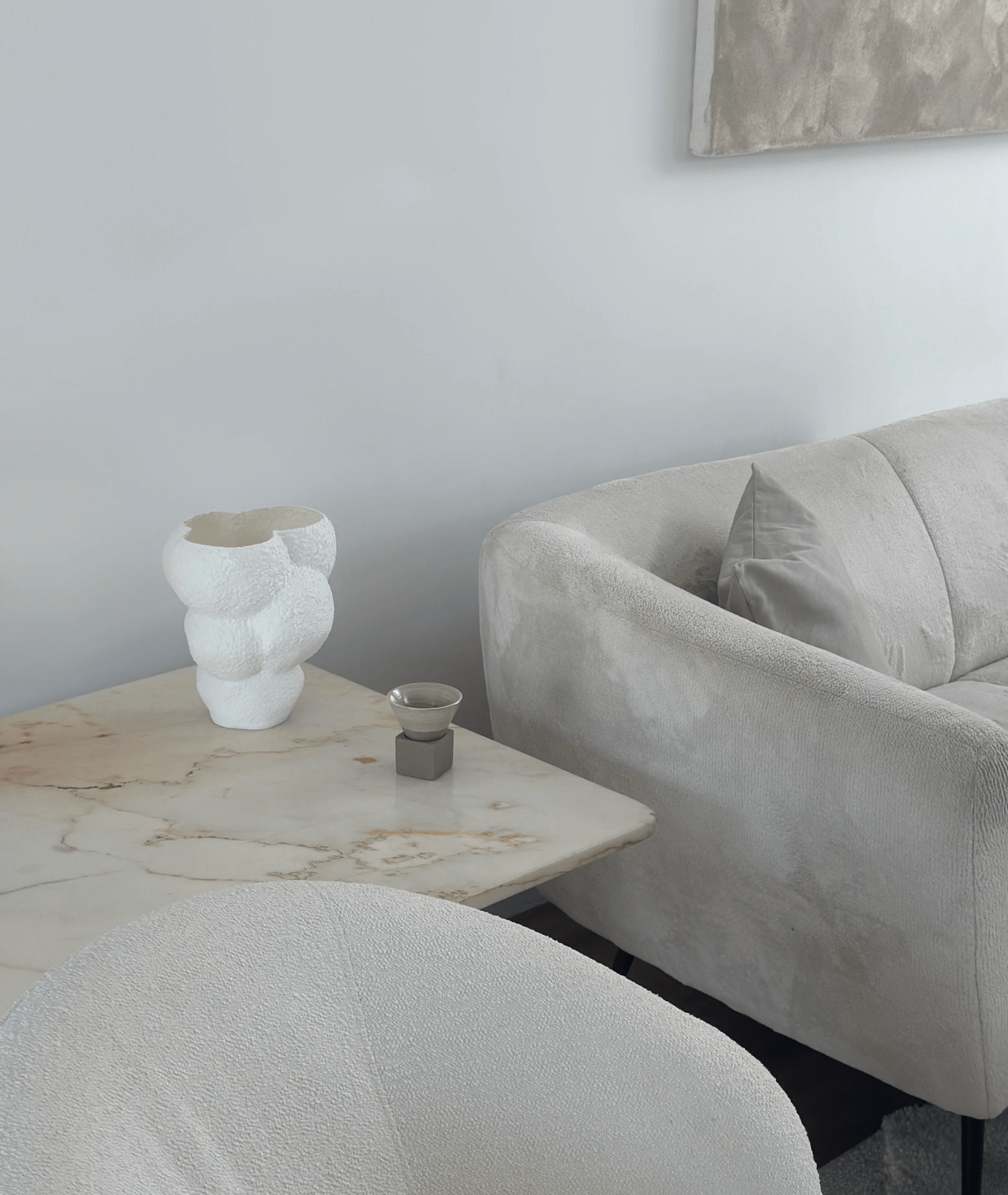 Minimalist living room with cream sofa, marble table, and unique white sculpture for contemporary decor.