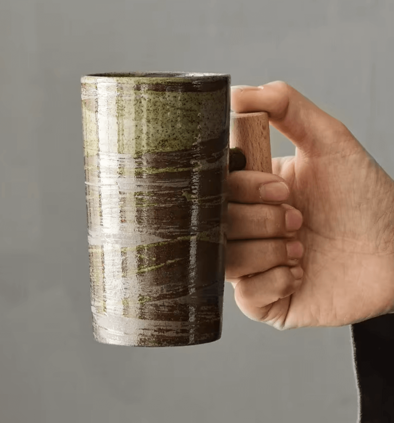 Hand holding a ceramic coffee mug with a natural wood handle, showcasing its rustic charm and modern design for enjoying hot beverages.
