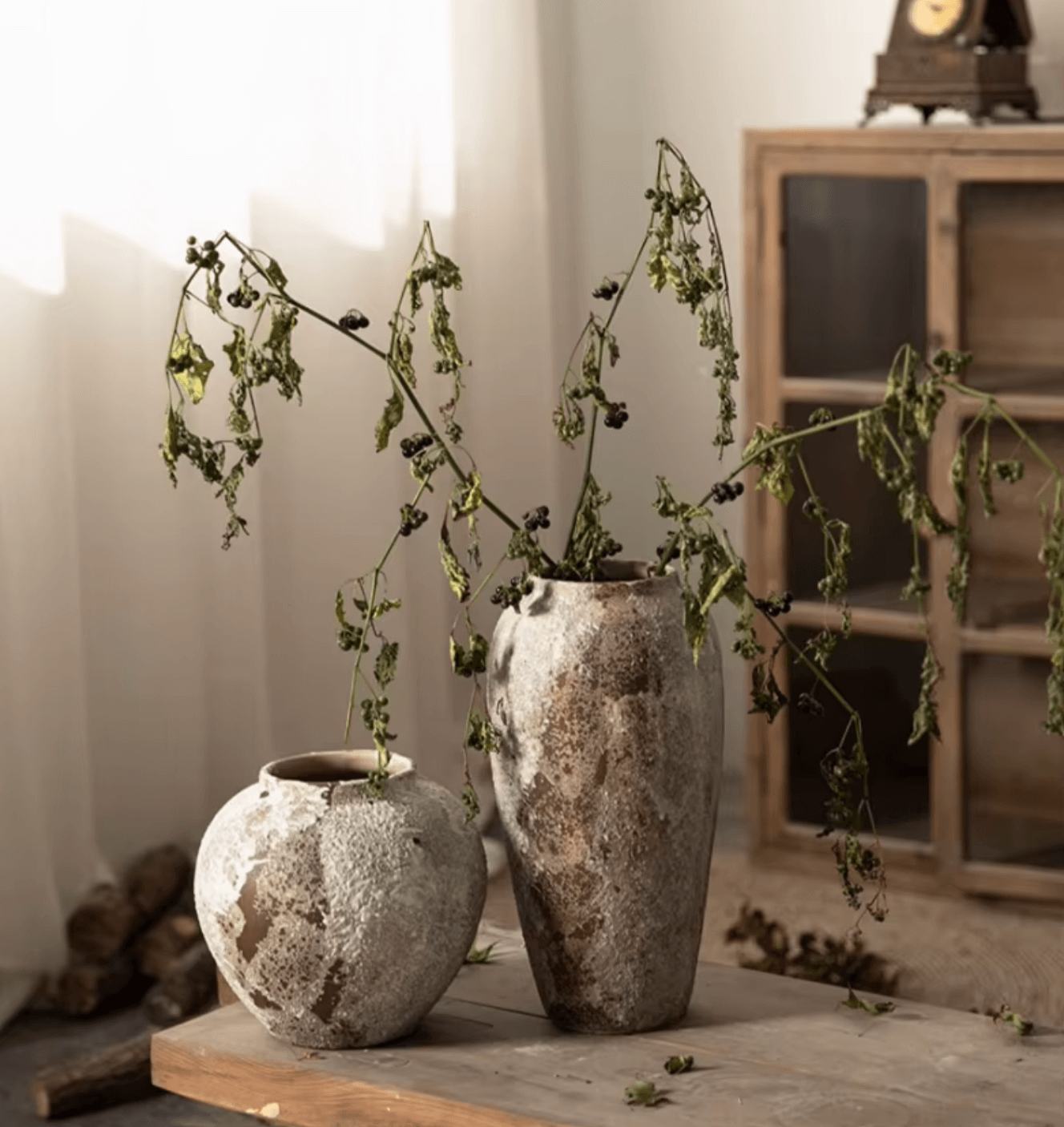 Zwei handgefertigte Keramikvasen im rustikalen antiken Design auf einem Holztisch, mit verblühten Zweigen dekoriert.