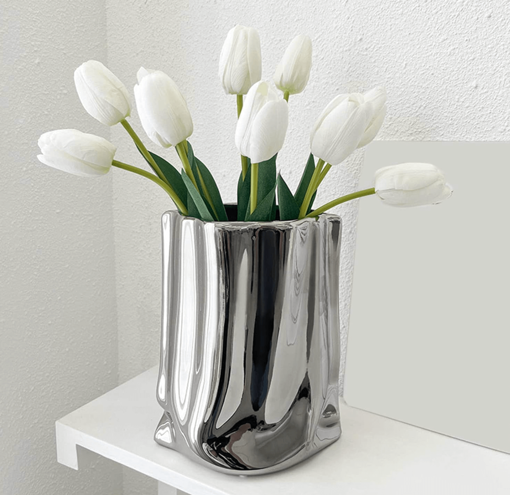 Silberne Blumenvase aus Keramik auf Regal mit weißen Tulpen, elegante Dekoration für stilvolle Arrangements im modernen Design.