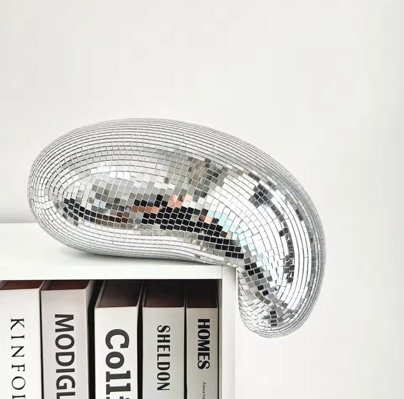 Melting disco ball with mirror tiles as stylish decor on bookshelf