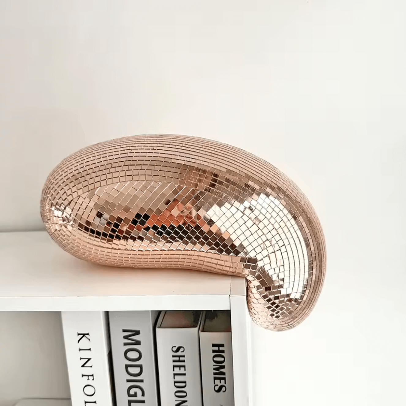 Stylish melting disco ball decor with mirrored tiles on a bookshelf, adding retro glamour to a modern room.