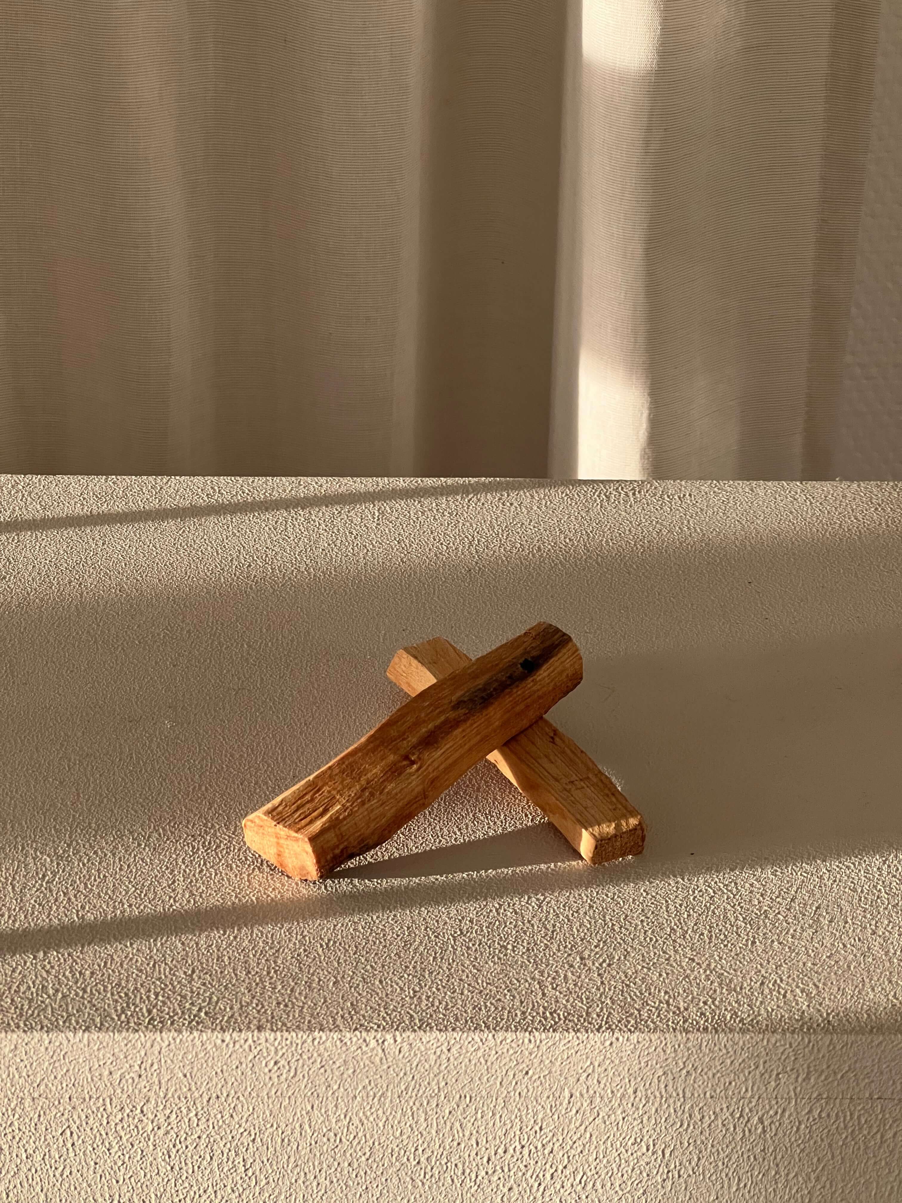 Two Palo Santo sticks for spiritual cleansing and harmony on a textured surface, sunlight casting soft shadows.