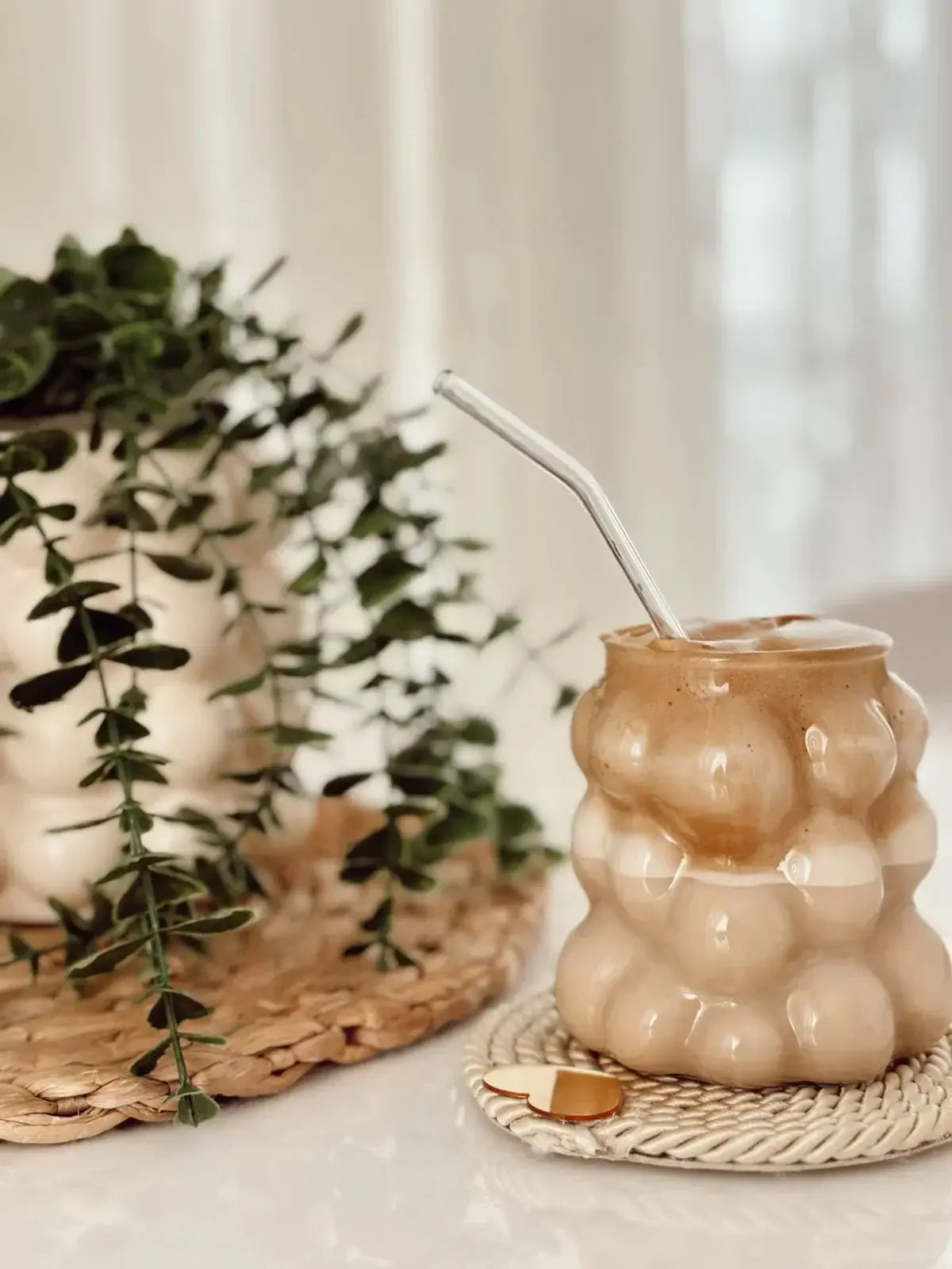 Elegant ceramic mug with a unique bubble design, filled with coffee and adorned with a metal straw, placed on a straw coaster next to greenery.