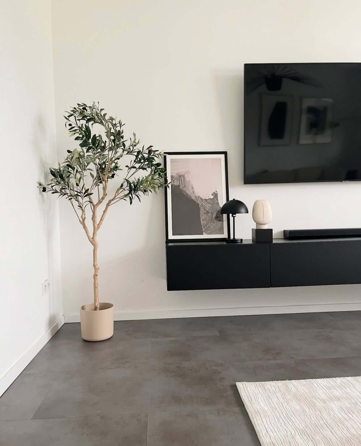 Artificial olive tree in a modern living room next to a black TV console, adding a touch of Mediterranean elegance without maintenance.