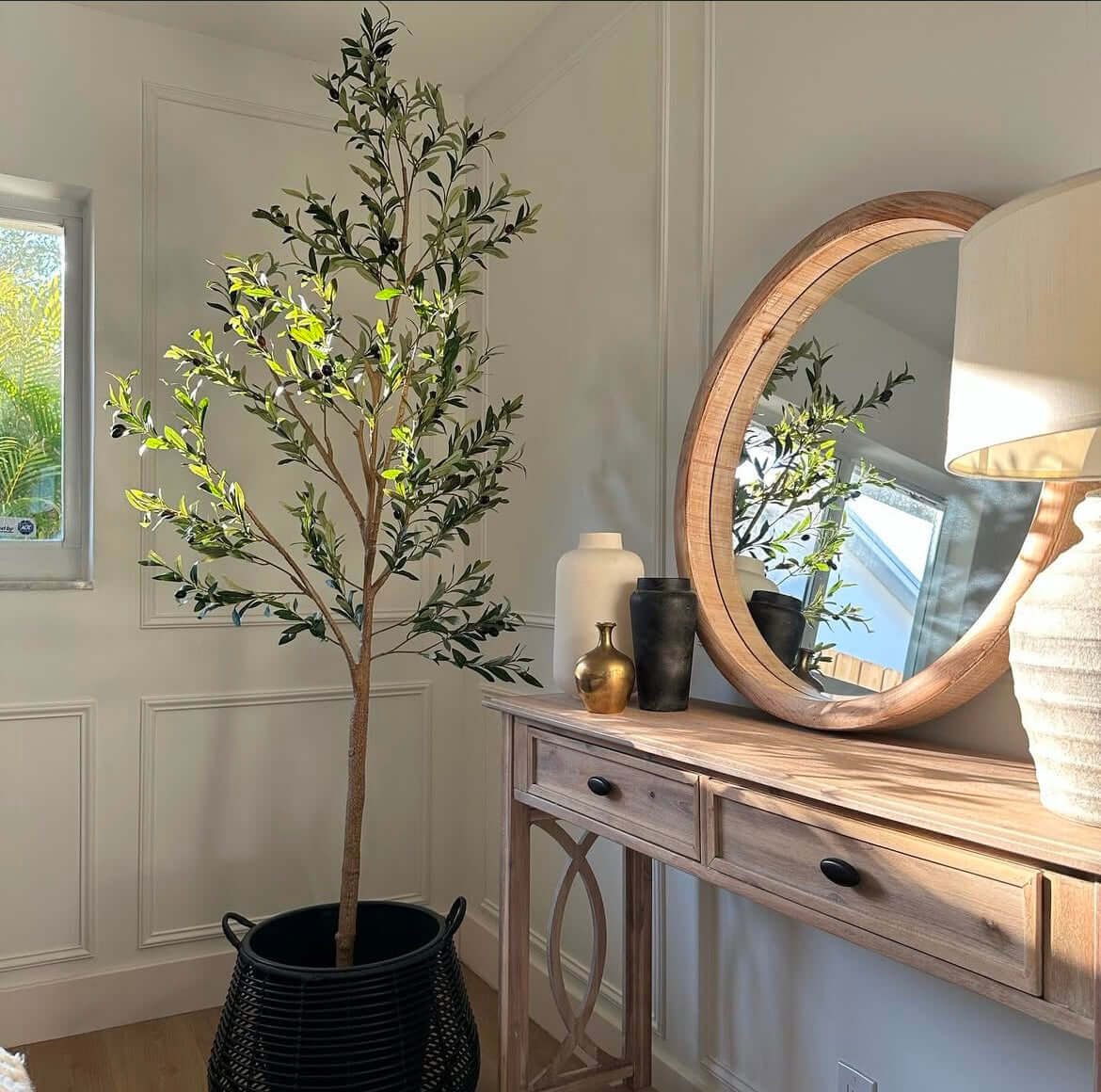Künstlicher Olivenbaum in modernem Raum, dekoriert mit Spiegel und Holzkonsole, bringt mediterrane Eleganz ohne Pflegeaufwand.