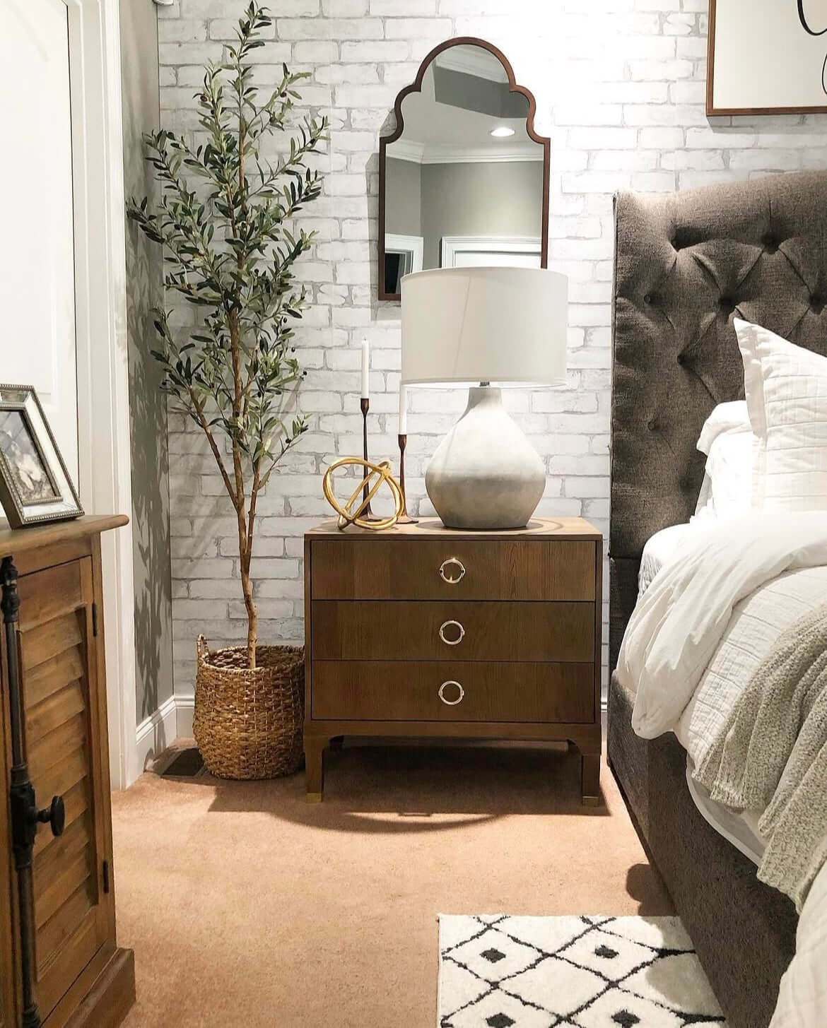 Stylish bedroom featuring a potted artificial olive tree next to a wooden nightstand and a decorative lamp.