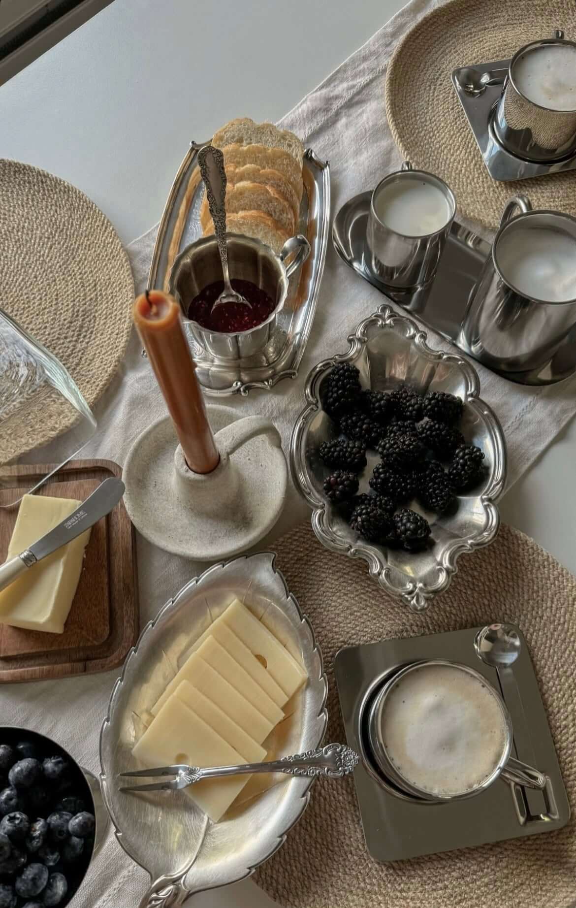 Elegant table setting with blackberries, cheese, bread, and stainless steel coffee set.