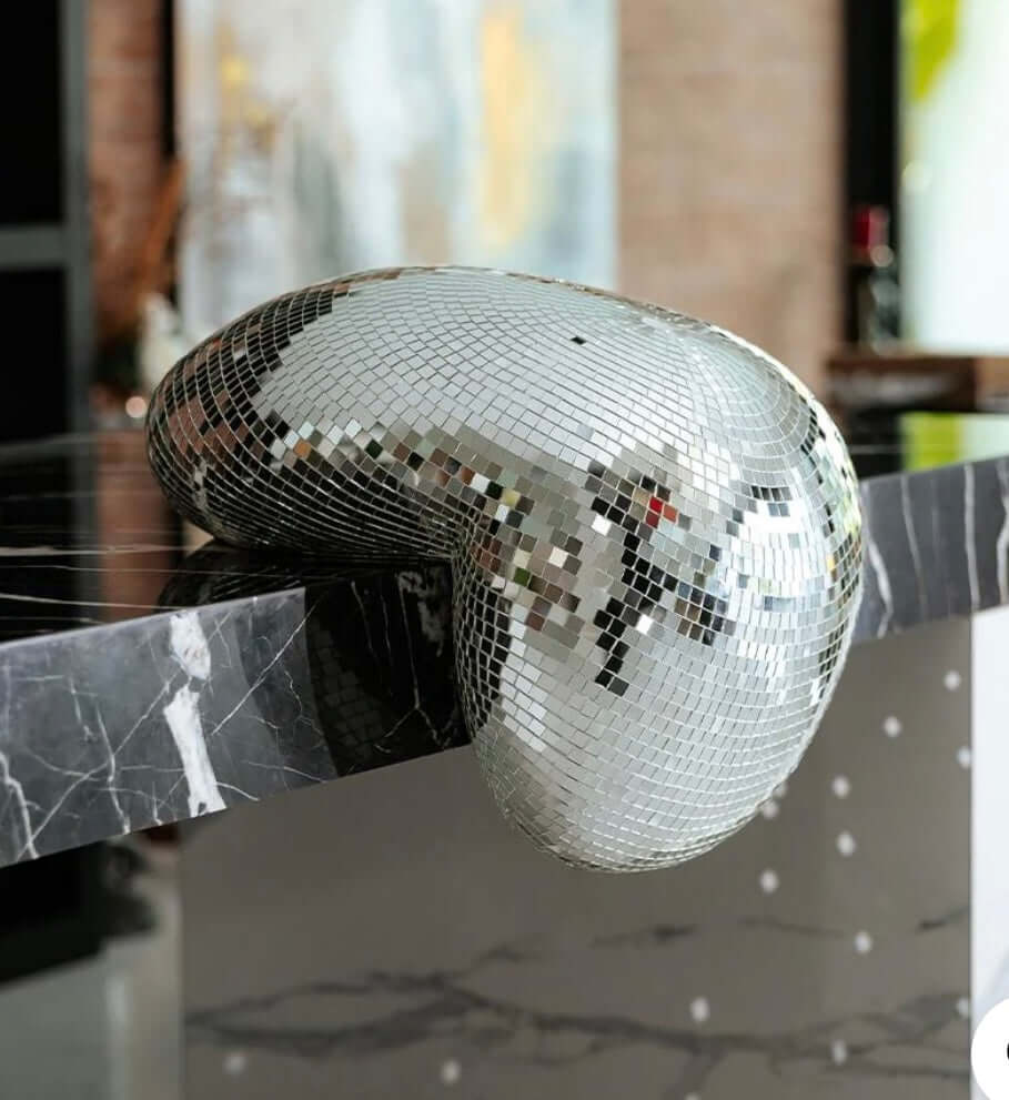 Stylish melting disco ball decor piece on a marble surface showcasing retro-glamour with mirrored tiles and modern design.