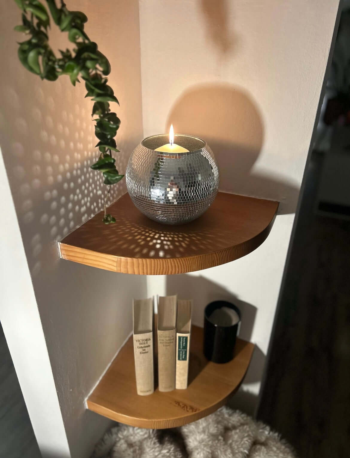 Disco ball flower pot with glowing candle on wooden shelf, reflecting light on wall and adding elegant decor to home space.