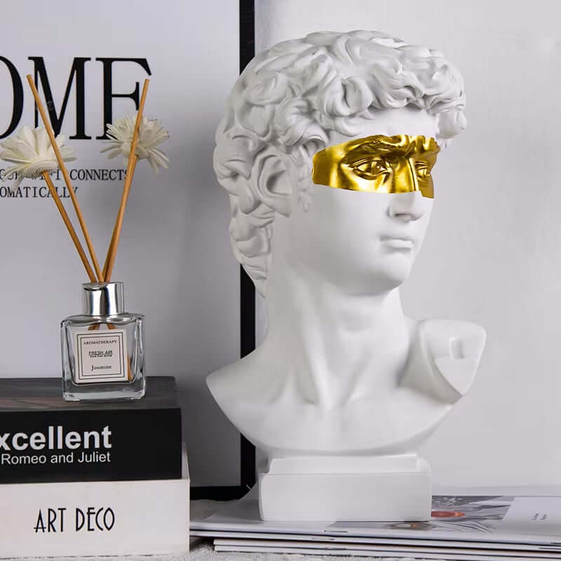 Modern David-head sculpture with gold mask, blending Renaissance and modern design, displayed on a shelf with decor.