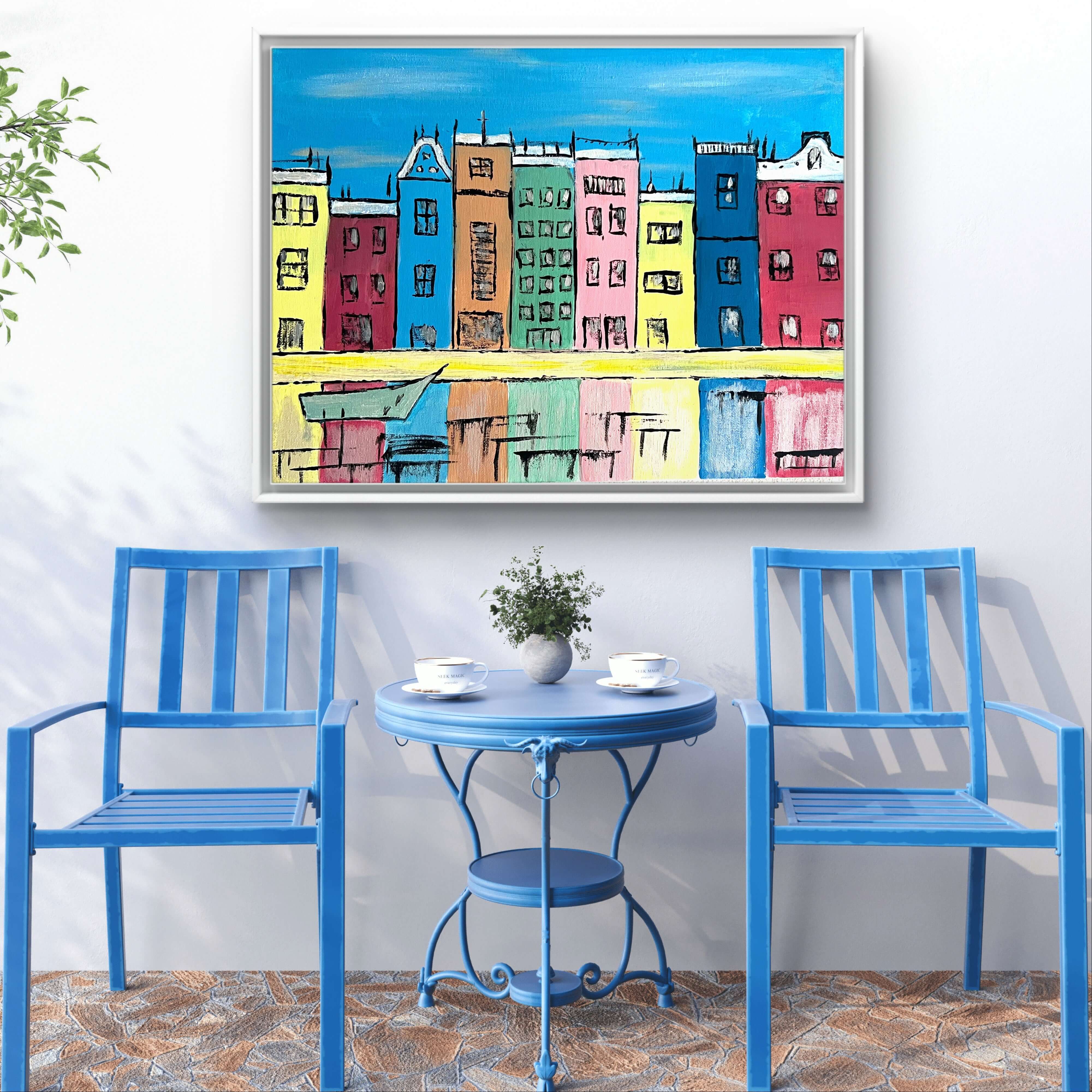 Colorful painting of Amsterdam houses in black frame on wall above blue outdoor furniture set.
