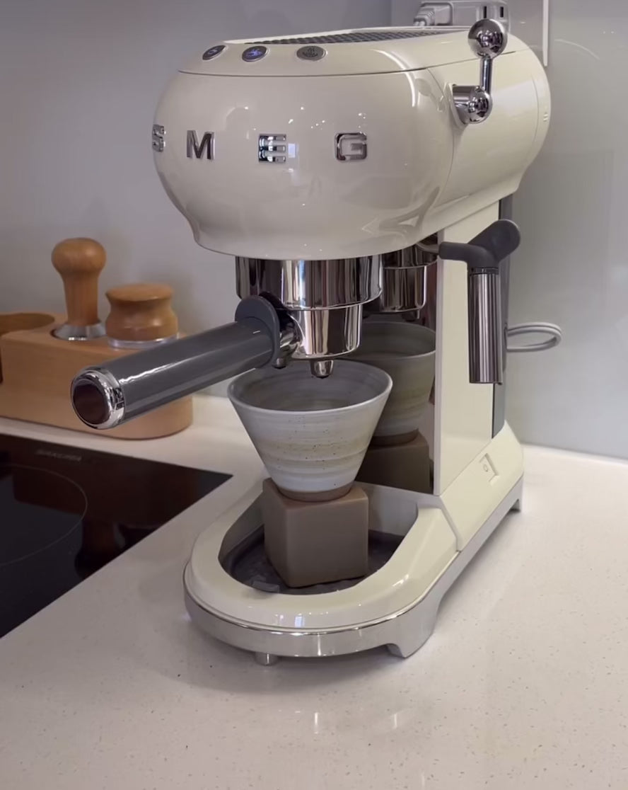 White espresso machine on a kitchen counter with chrome accents and a coffee cup in place.