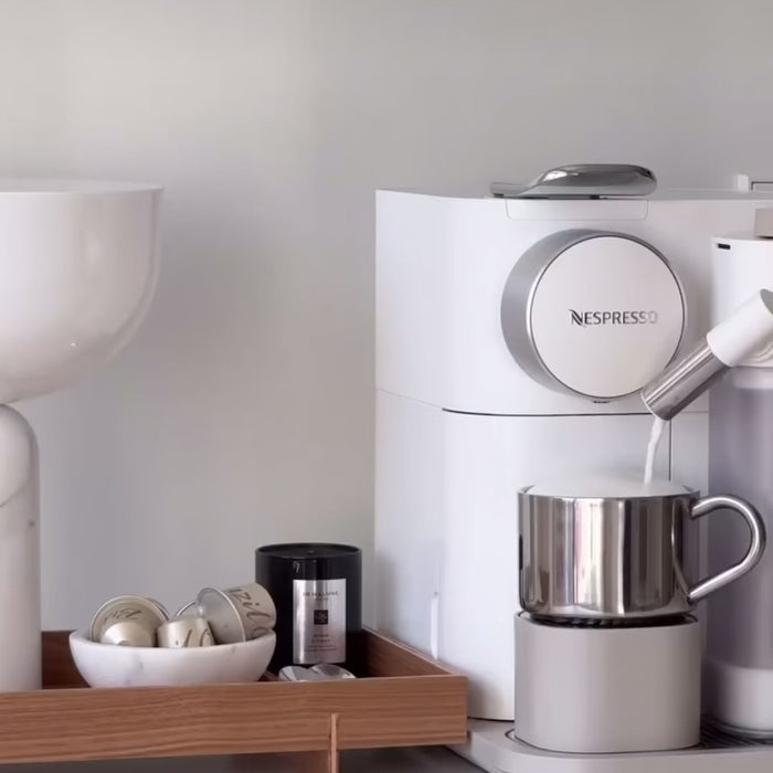 Modern coffee machine with stainless steel cup on tray, featuring sleek design and capsules, ideal for home office use.