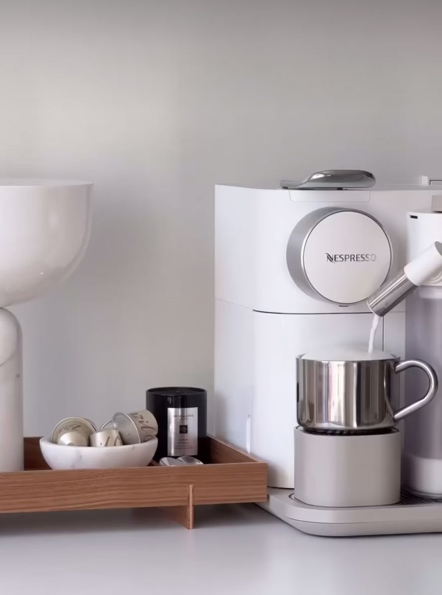 Modern coffee machine with stainless steel cup on tray, featuring sleek design and capsules, ideal for home office use.