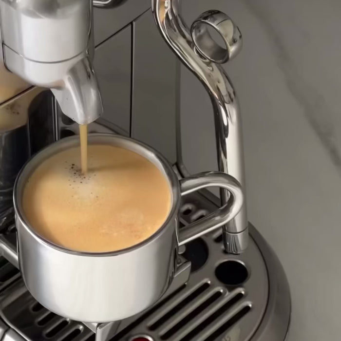 Espresso being prepared in a sleek, stainless steel coffee maker with a double-wall design.
