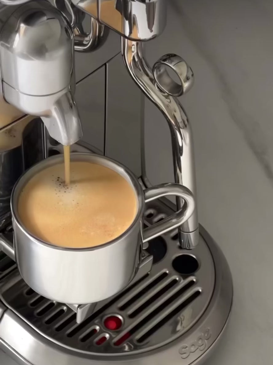 Espresso being prepared in a sleek, stainless steel coffee maker with a double-wall design.